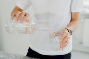 Person gießt Wasser in ein Glas